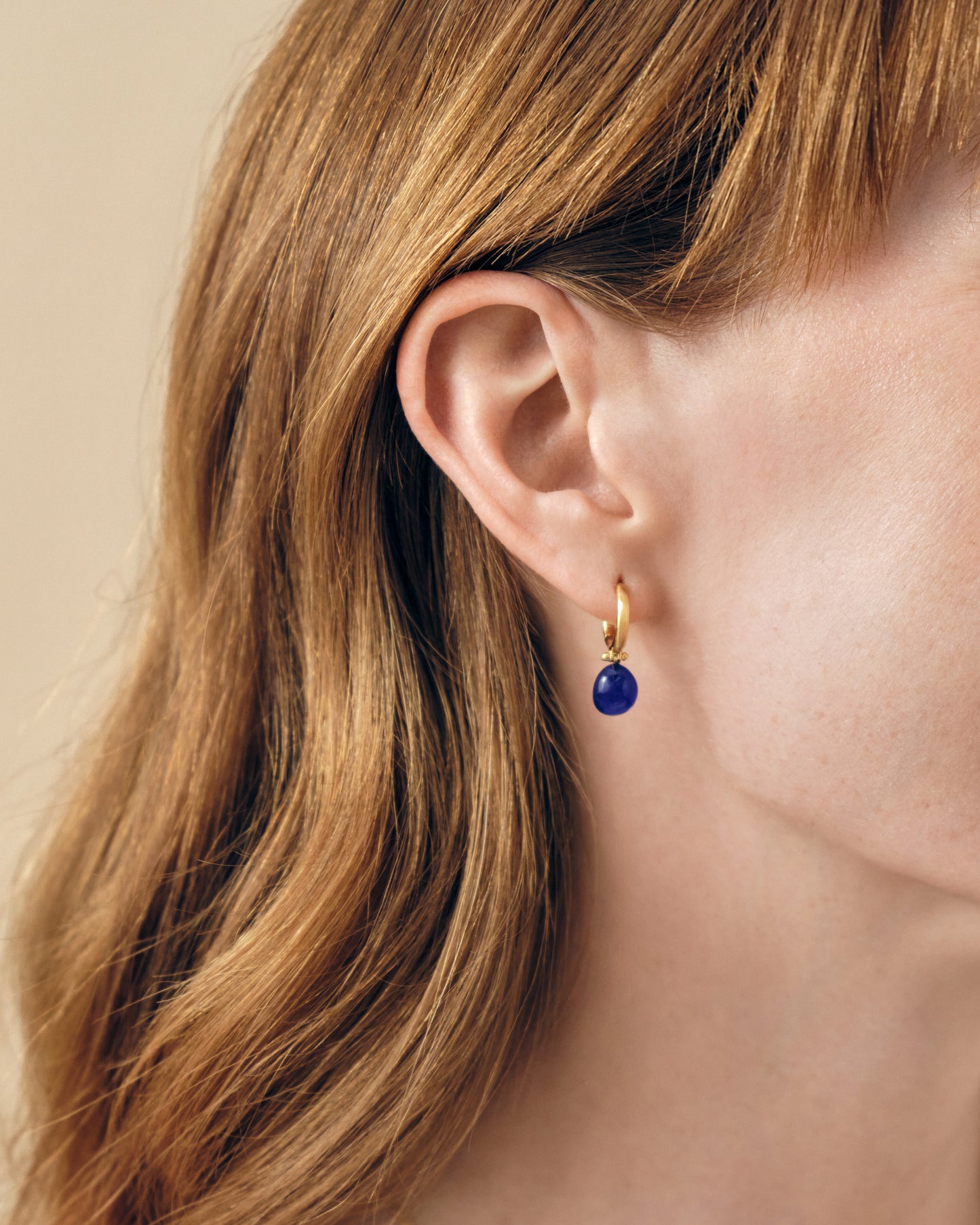 Close-up of a woman wearing Coastal Blue Quartz Earrings featuring gold-plated sterling silver hoops with a deep blue quartz stone, crafted using recycled metals for ethical fine jewellery.