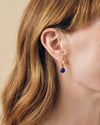 Close-up of a woman wearing Coastal Blue Quartz Earrings featuring gold-plated sterling silver hoops with a deep blue quartz stone, crafted using recycled metals for ethical fine jewellery.