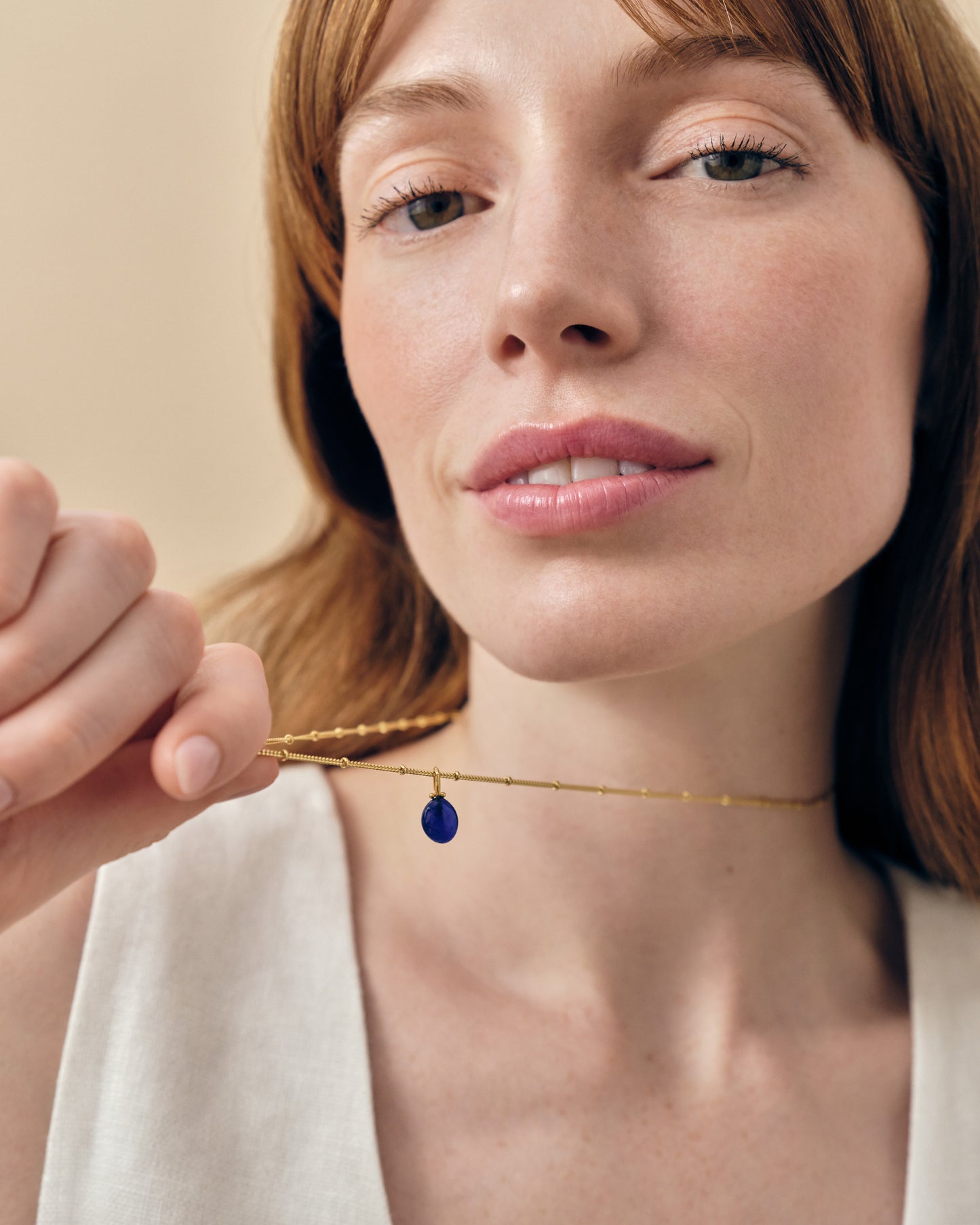 Close-up of a woman holding a Coastal Blue Quartz Necklace with a gold-plated chain and a deep blue quartz pendant, showcasing considered jewellery made with recycled metals.