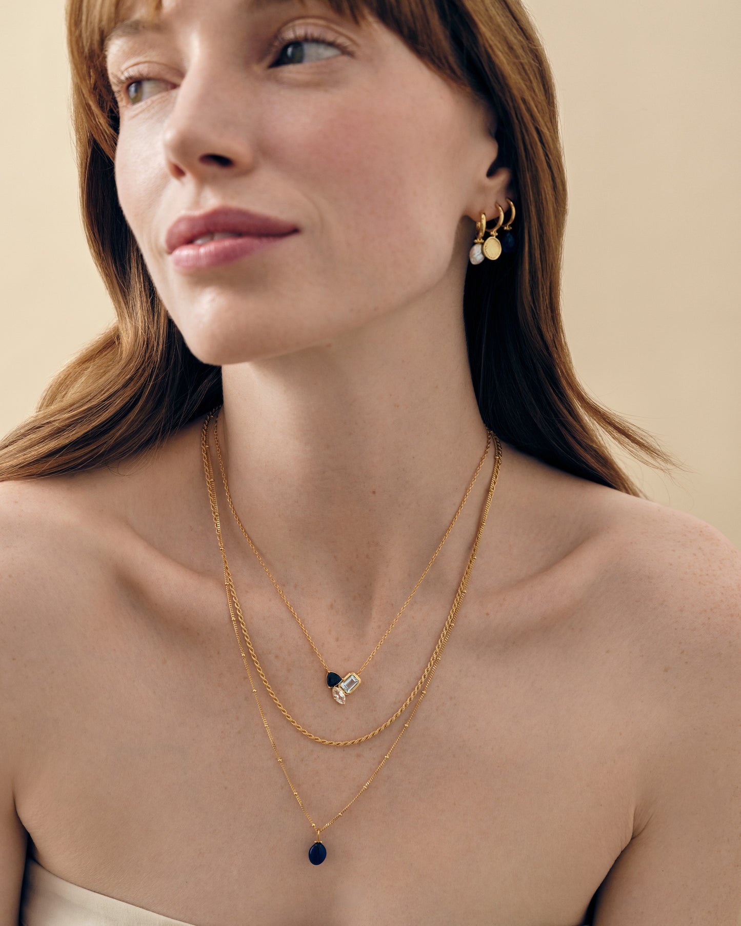 Woman wearing layered gold chain necklaces featuring the Coastal Blue Quartz Necklace with blue quartz pendant, styled with gold-plated and sterling silver earrings, showcasing ethical fine jewellery made from recycled metals and solid gold.