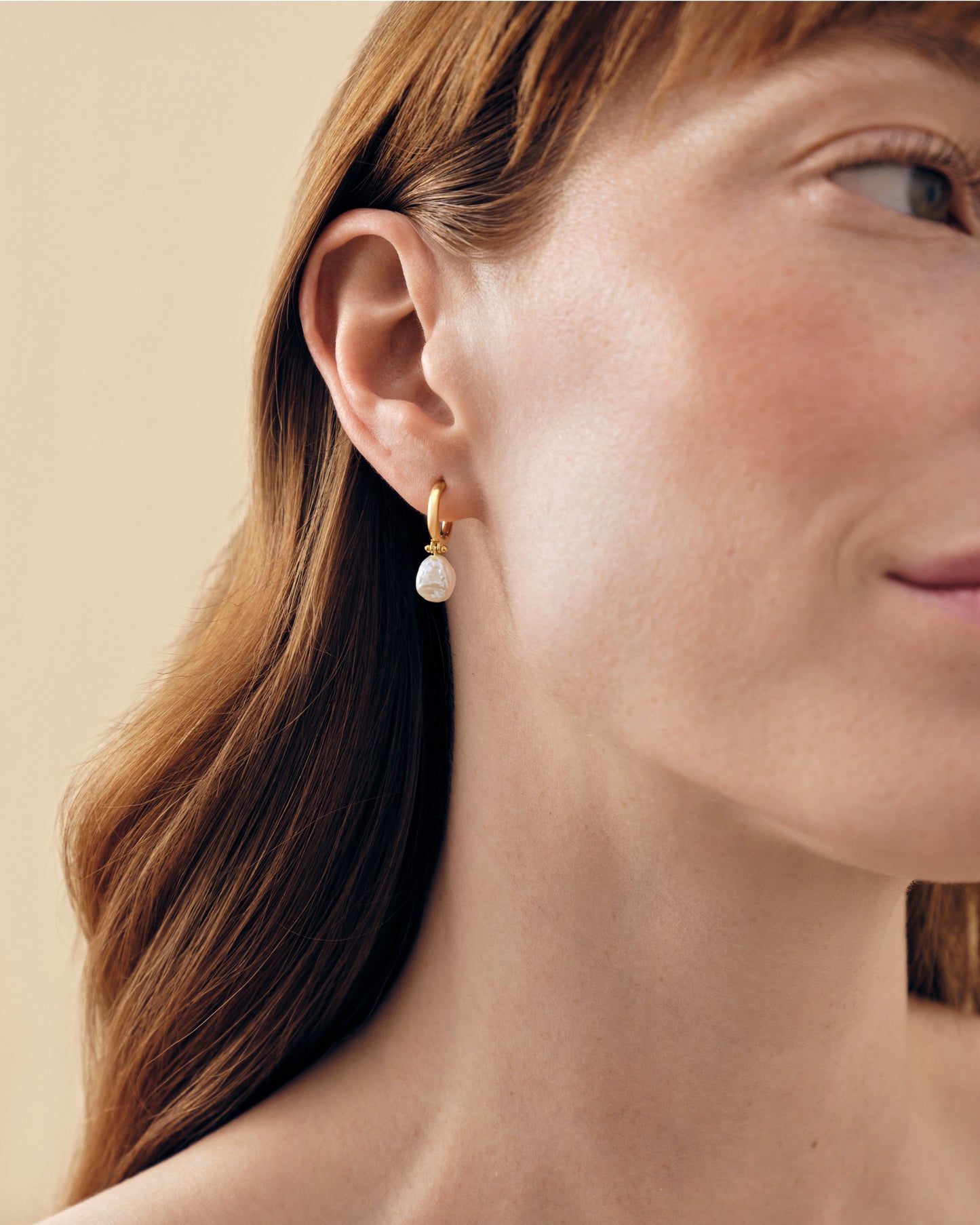 Close-up of a woman wearing Coastal Pearl Earrings, showcasing gold-plated stud design with a delicate pearl drop, crafted from sterling silver and recycled metals for everyday fine jewellery.