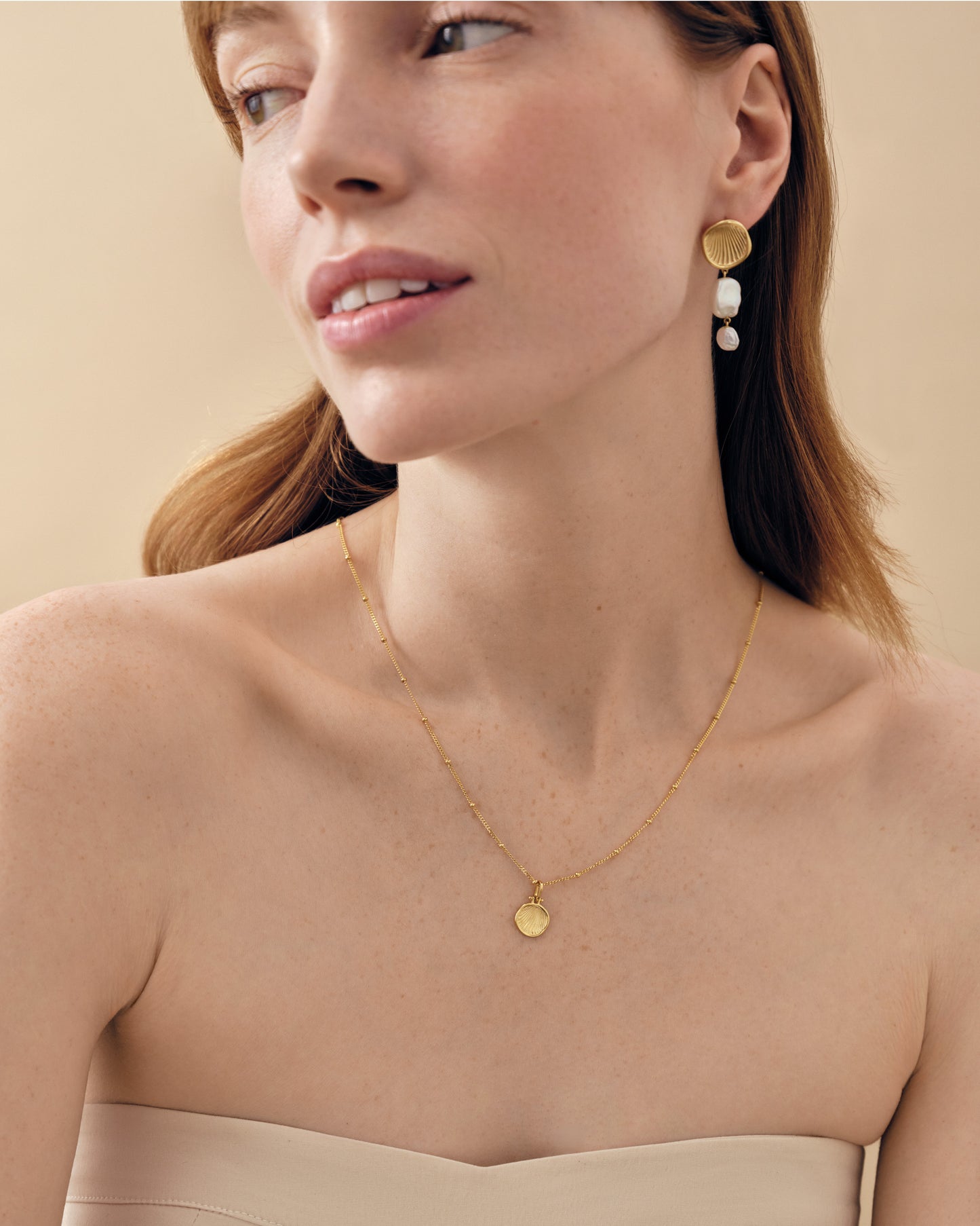 A close-up of a woman wearing Coastal Pearl Statement Earrings featuring gold-plated stud design with pearls, paired with a delicate gold necklace, showcasing fine jewellery made from recycled metals.