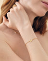 Close-up of a woman's wrist wearing the Coastal Shell Bracelet, a delicate gold-plated chain with a small shell charm, showcasing sustainable, considered luxury in recycled metals.