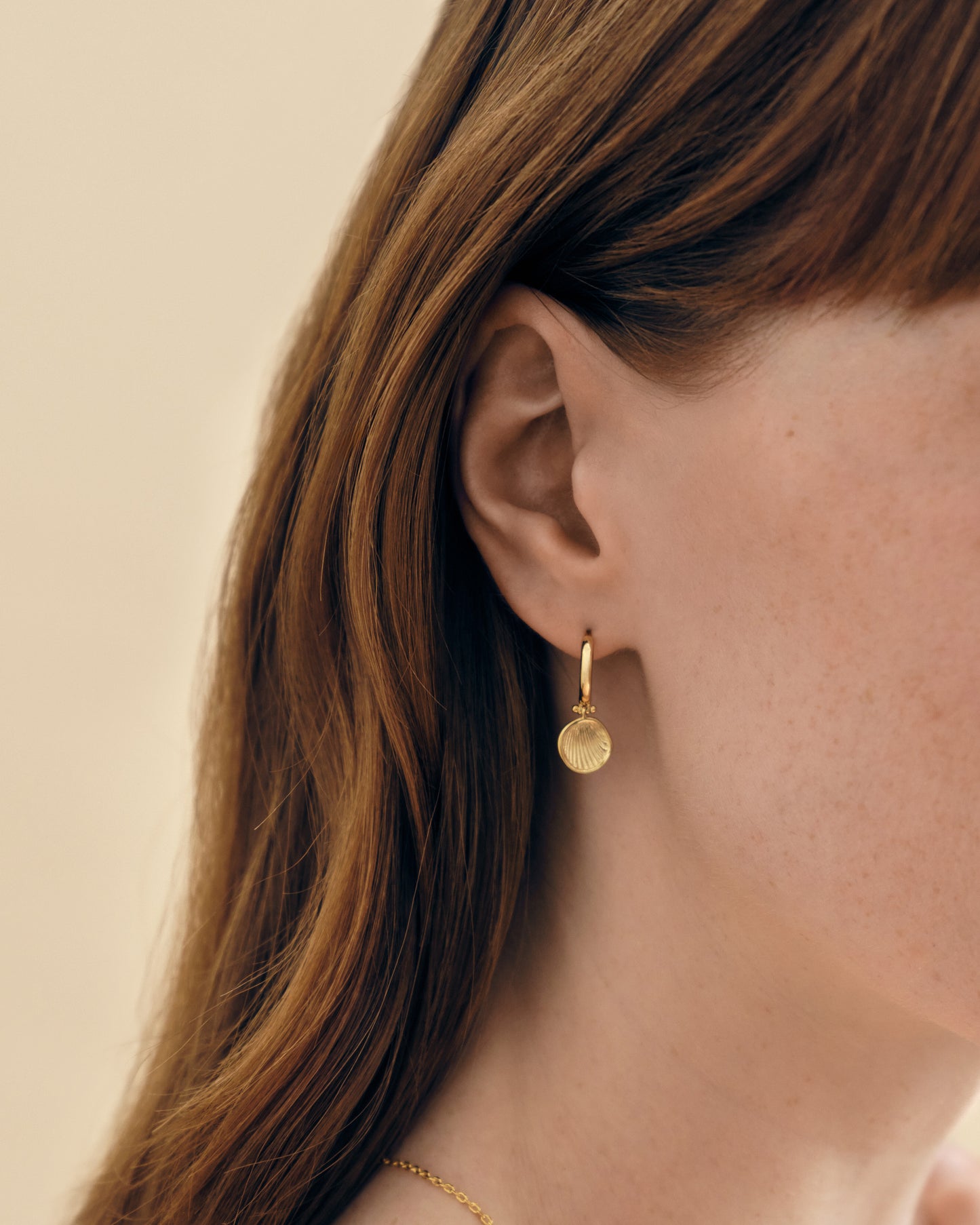 Close-up of a woman wearing Coastal Shell Earrings, gold-plated stud earrings featuring a delicate shell charm, crafted from recycled metals and ethical sourcing.