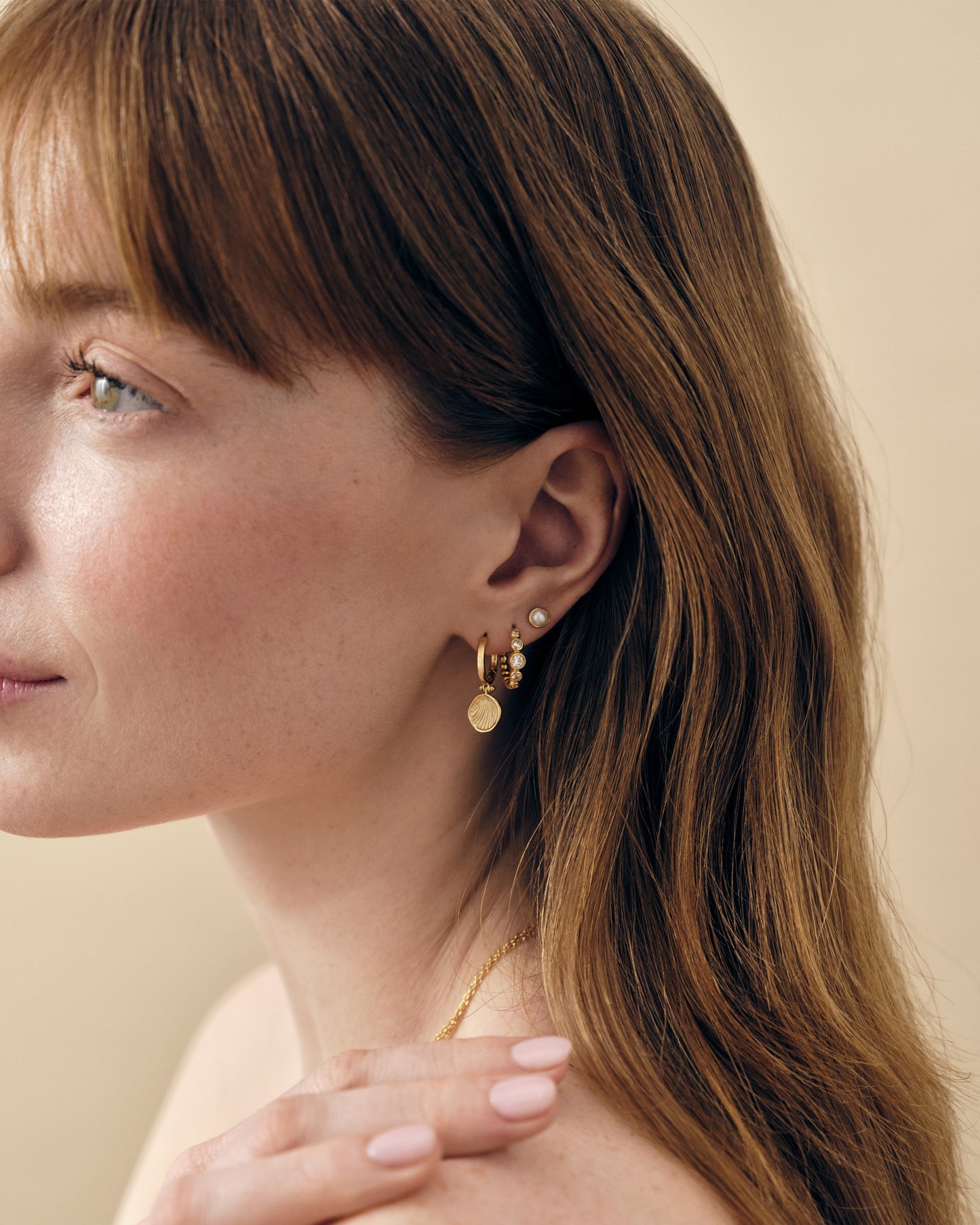 Close-up of a woman wearing Coastal Shell Earrings in gold-plated sterling silver, styled with additional gold and diamond stud earrings, showcasing considered jewellery made from recycled metals and ethical sourcing.