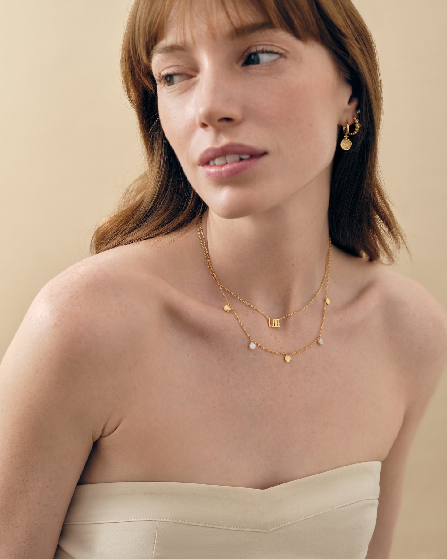 Woman wearing the Coastal Shell and Pearl Station Necklace, a delicate gold-plated and sterling silver chain with subtle shell and pearl pendants, showcasing sustainable fine jewellery made from recycled metals and ethically sourced materials.