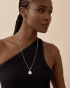 A close-up of a woman wearing the Coin Globe Necklace - Silver, featuring a sterling silver pendant and chain, showcasing considered jewellery crafted from recycled metals with ethical sourcing.