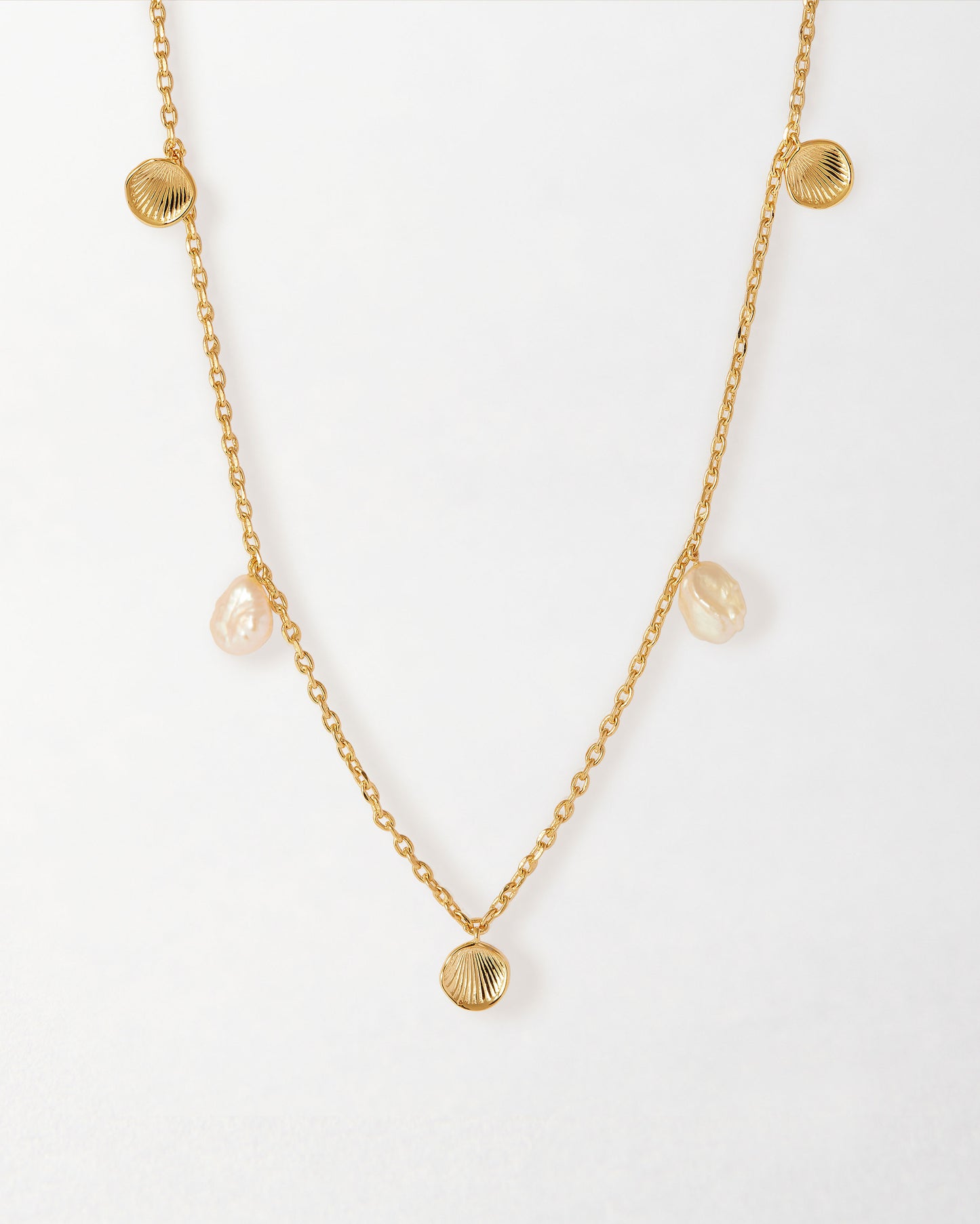 Delicate Coastal Shell and Pearl Station Necklace featuring gold-plated chain with pearl and shell-shaped pendants, crafted from recycled metals and built to last.