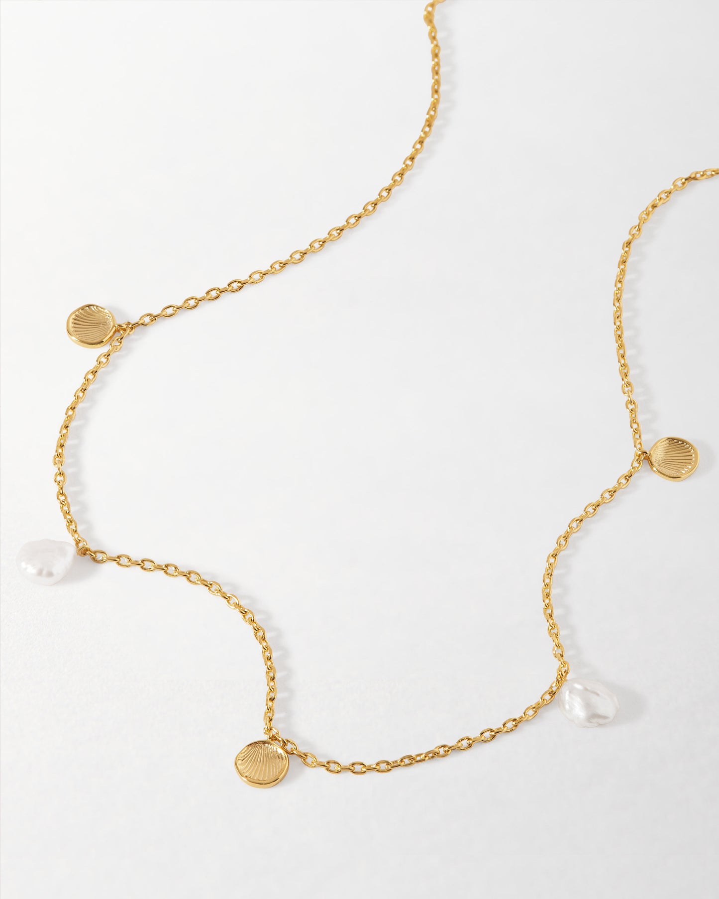 Coastal Shell and Pearl Station Necklace featuring gold-plated chain with delicate shell-shaped and pearl pendants, crafted from recycled metals for considered jewellery. Solid gold, fine jewellery for the everyday. Made to last.