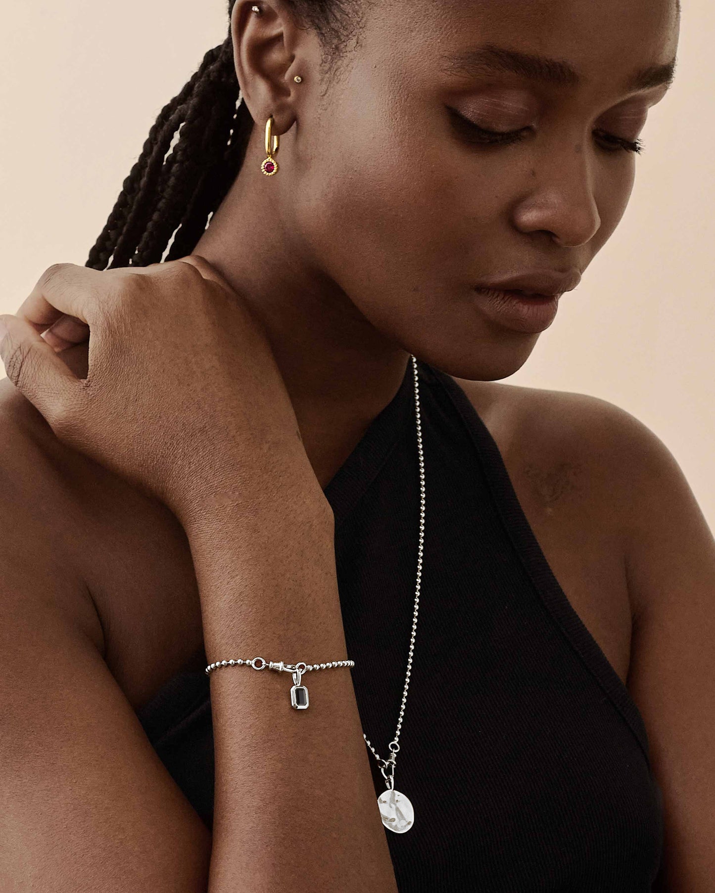 A close-up of a woman wearing the Deco Black Spinel Globe Bracelet - Silver made from sterling silver with a black spinel gemstone charm, paired with a minimalist chain necklace and gold hoop earrings, showcasing considered jewellery crafted from recycled metals and ethical sourcing.