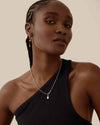 A woman wearing the Deco White Topaz Globe Necklace - Silver, featuring a sterling silver pendant and chain, styled with a black one-shoulder top, showcasing considered jewellery made in recycled metals.