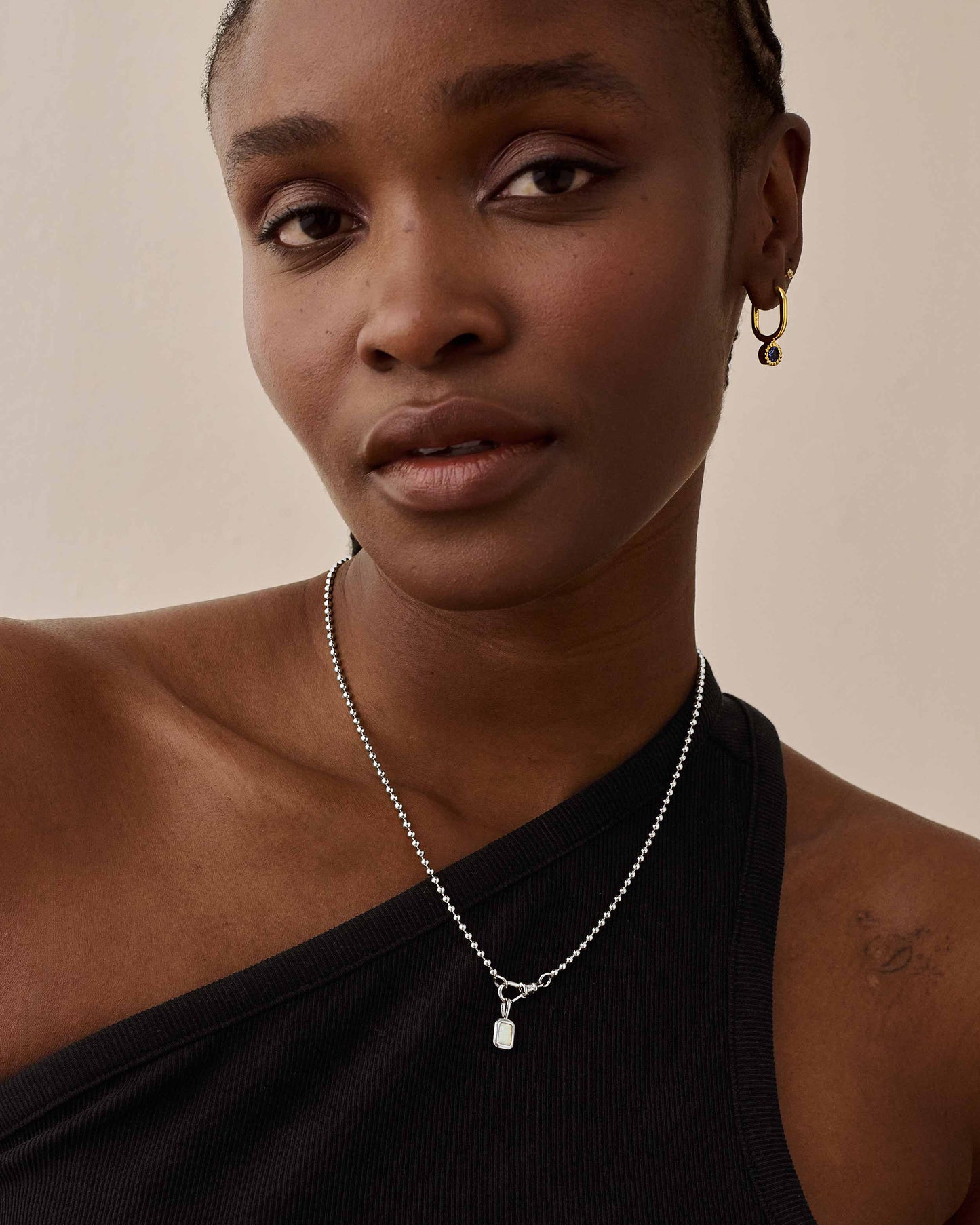 Close-up of a person wearing the Deco White Topaz Globe Necklace - Silver, featuring a sterling silver pendant and chain, styled with a black one-shoulder top, highlighting fine jewellery made from recycled metals that is built to last.