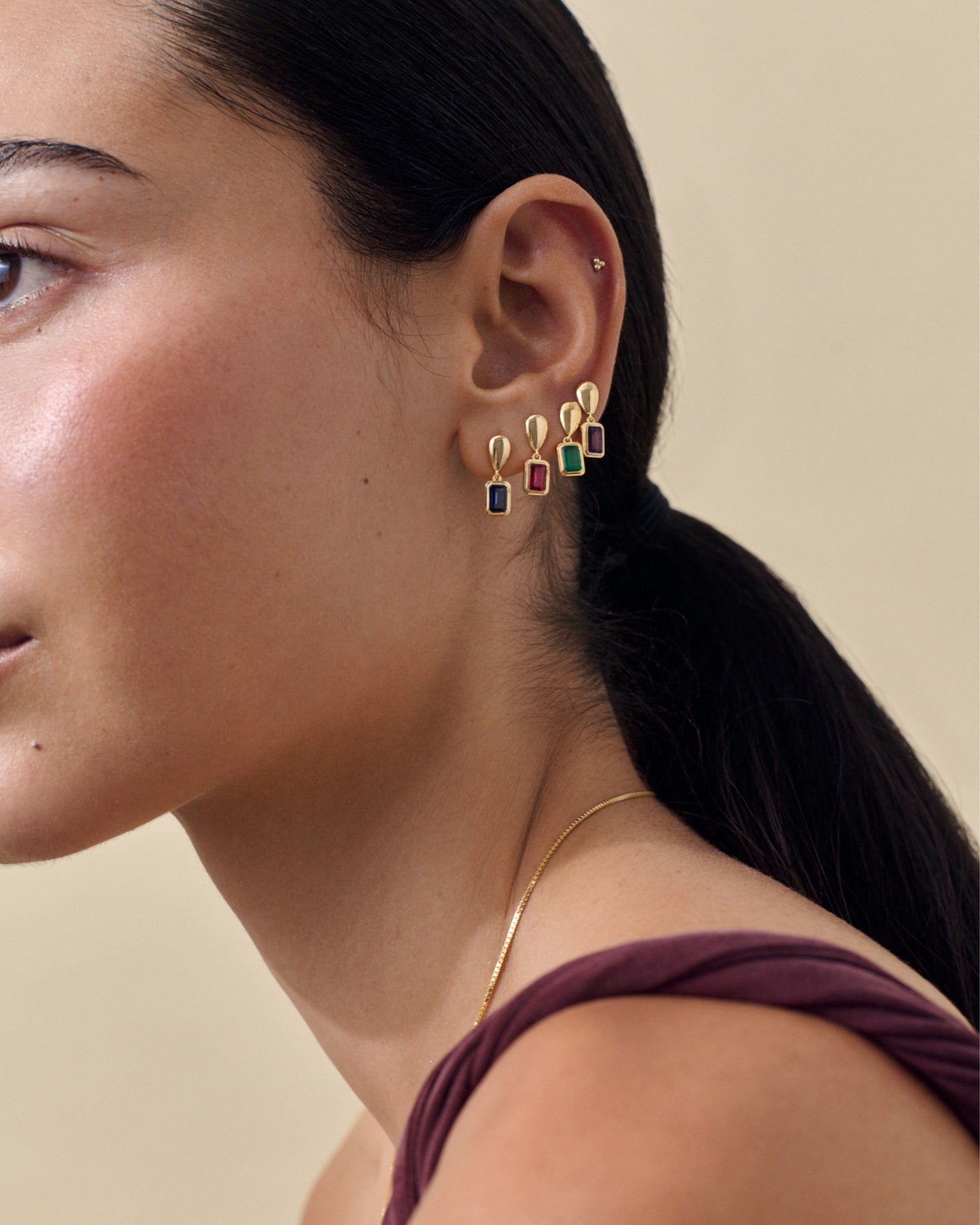 Close-up of a woman wearing Pebble Blue Sapphire September Birthstone Drop Earrings in gold-plated sterling silver, showcasing sustainable, ethically sourced fine jewellery crafted from recycled metals and solid gold.