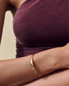 Close-up of a person wearing the Pebble Green Onyx Cuff, a gold-plated sterling silver cuff featuring a sleek design and a small green onyx stone, crafted with recycled metals for everyday fine jewellery.