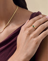 A close-up of a hand wearing the Pebble Green Onyx Ring in gold-plated sterling silver, paired with a gold necklace and a deep purple top, showcasing ethical, recycled metals and fine craftsmanship.