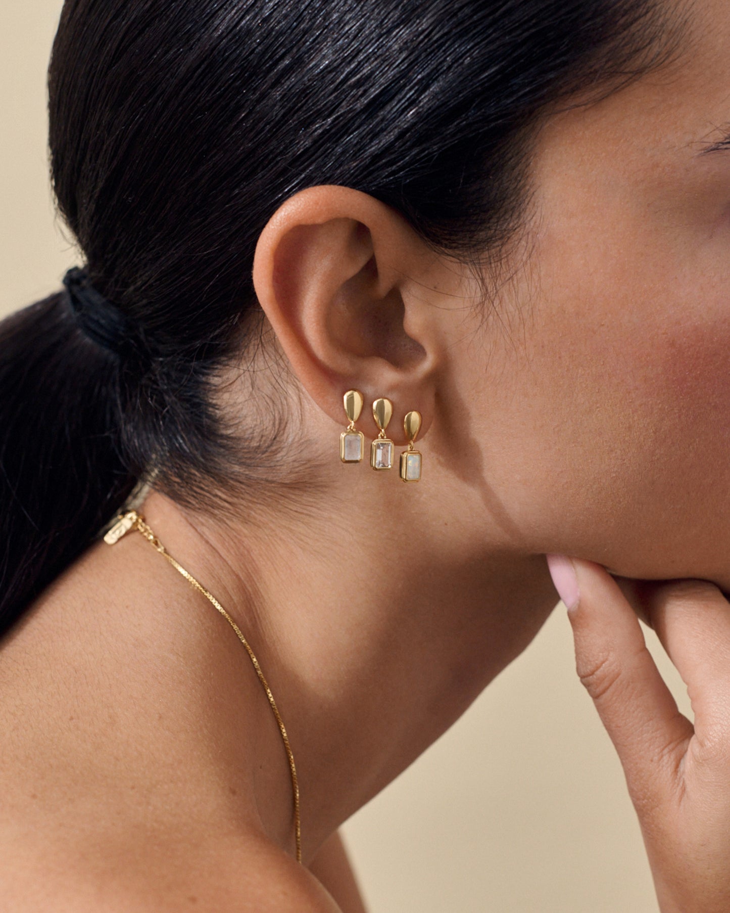 Close-up of a woman wearing Pebble Rainbow Moonstone June Birthstone Drop Earrings in gold-plated sterling silver, showcasing eco-friendly, fine jewellery crafted with recycled metals and ethical sourcing.