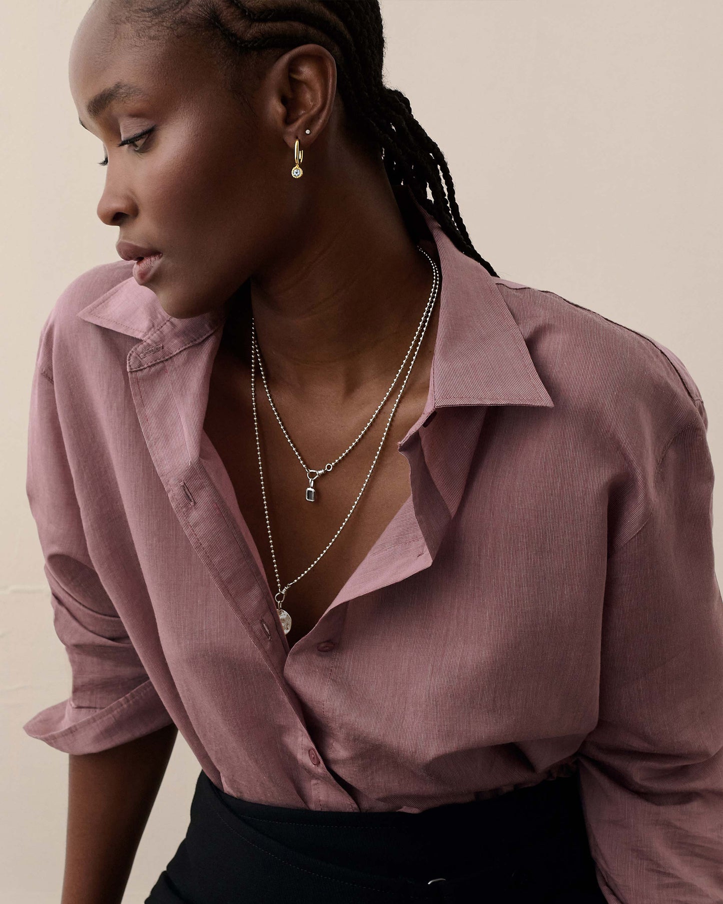 A woman wearing layered sterling silver pendant necklaces featuring the Deco Black Spinel Globe Necklace - Silver, paired with a mauve button-up shirt, showcasing elegant sustainable fine jewellery.