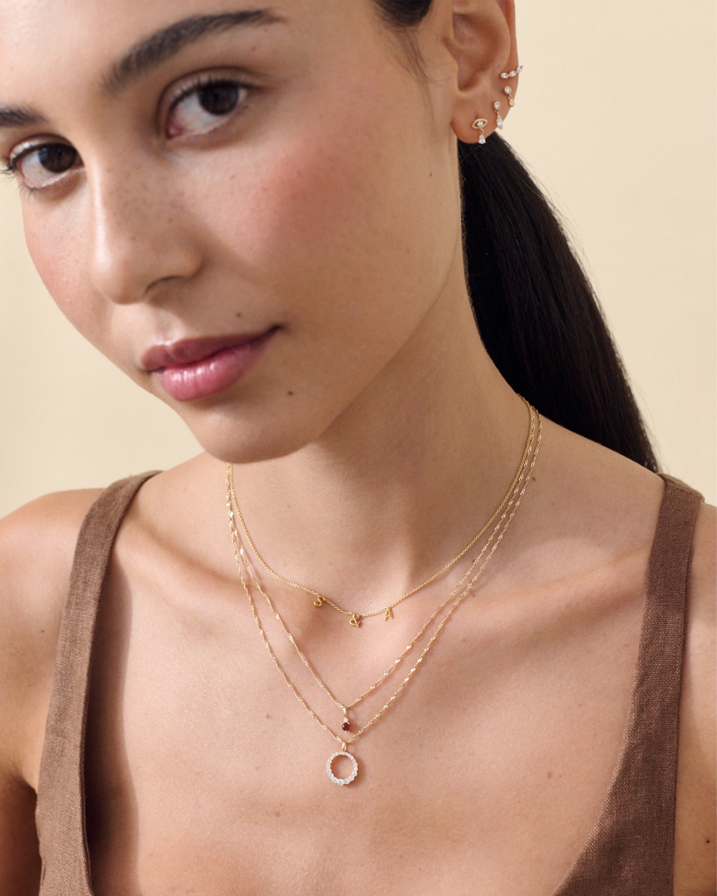 Close-up of a woman wearing the Diamond Halo Necklace pendant in solid 14ct gold with diamonds, styled with layered fine gold chains, showcasing considered jewellery crafted from recycled metals and ethically sourced materials.