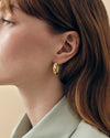 Close-up of a woman wearing Charlotte Collins Dome Triple Pavé Hoop Earrings in gold-plated and silver, showcasing fine craftsmanship and ethical, recycled metals for everyday luxury.