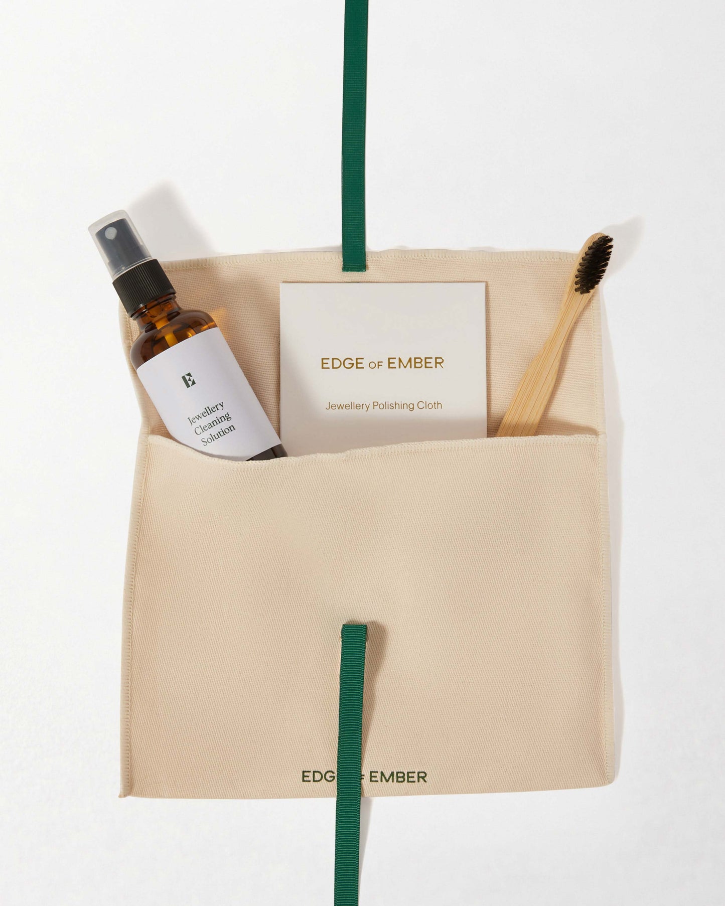 Jewellery Care Kit neatly arranged with a polishing cloth, cleaning solution spray, and wooden brush in a beige pouch, reflecting considered jewellery made in recycled metals.