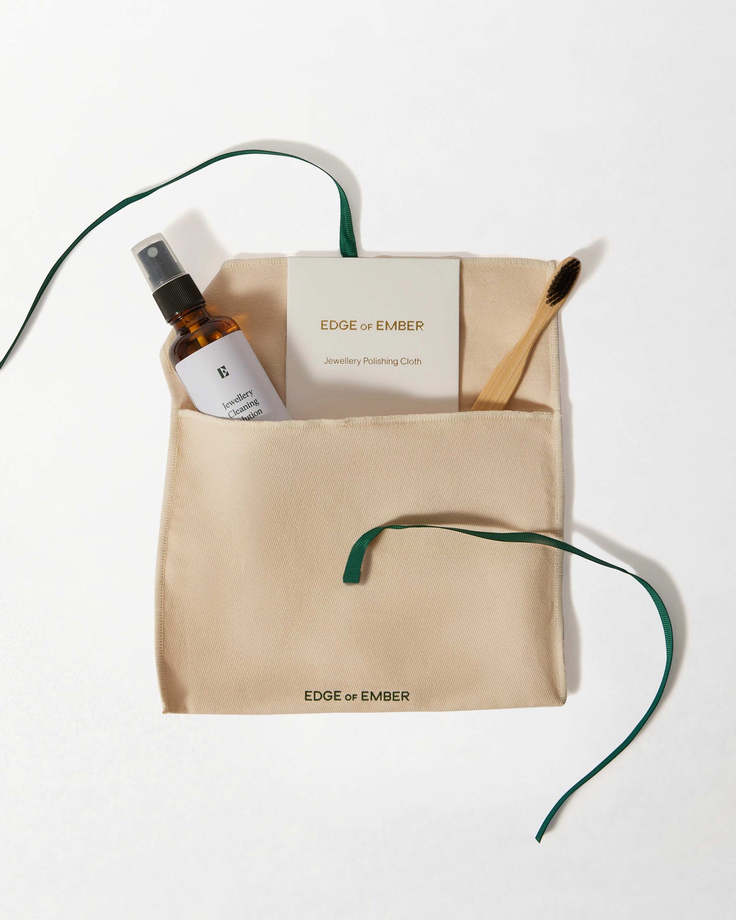 Jewellery Care Kit featuring a polishing cloth, cleaning spray, and bamboo brush neatly arranged in a beige pouch with green tie, crafted for solid gold and lab-grown diamond jewellery care.