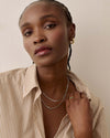Woman wearing the Globe Chain Necklace - Silver made from sterling silver, styled with layered chains and a green onyx ring, showcasing elegant sustainable fine jewellery crafted from recycled metals.
