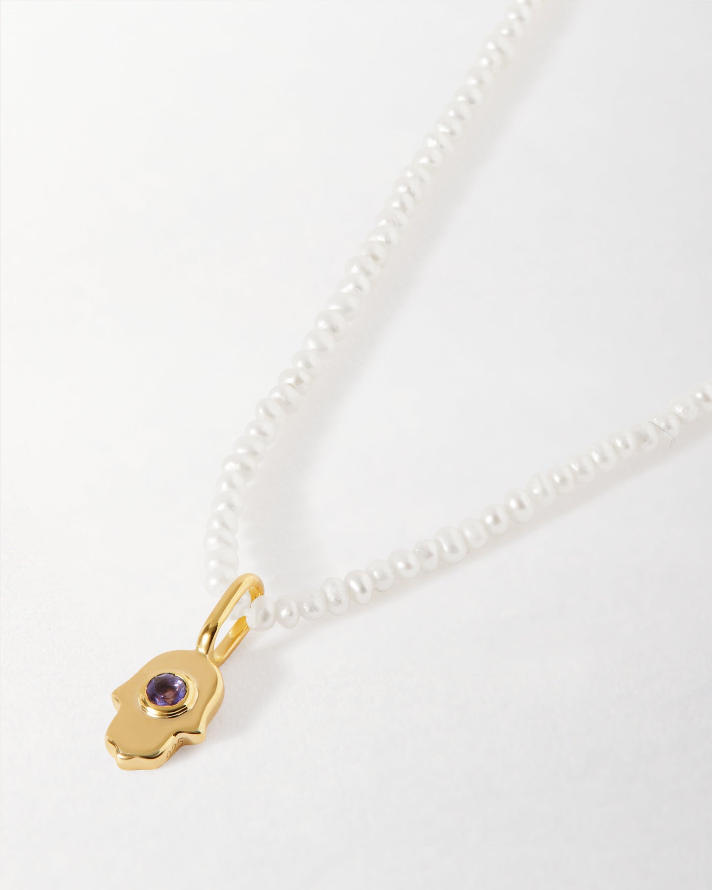 Mini Hamsa Pearl Necklace featuring a gold-plated pendant with a purple gemstone and delicate sterling silver chain, crafted in recycled metals and fine craftsmanship.