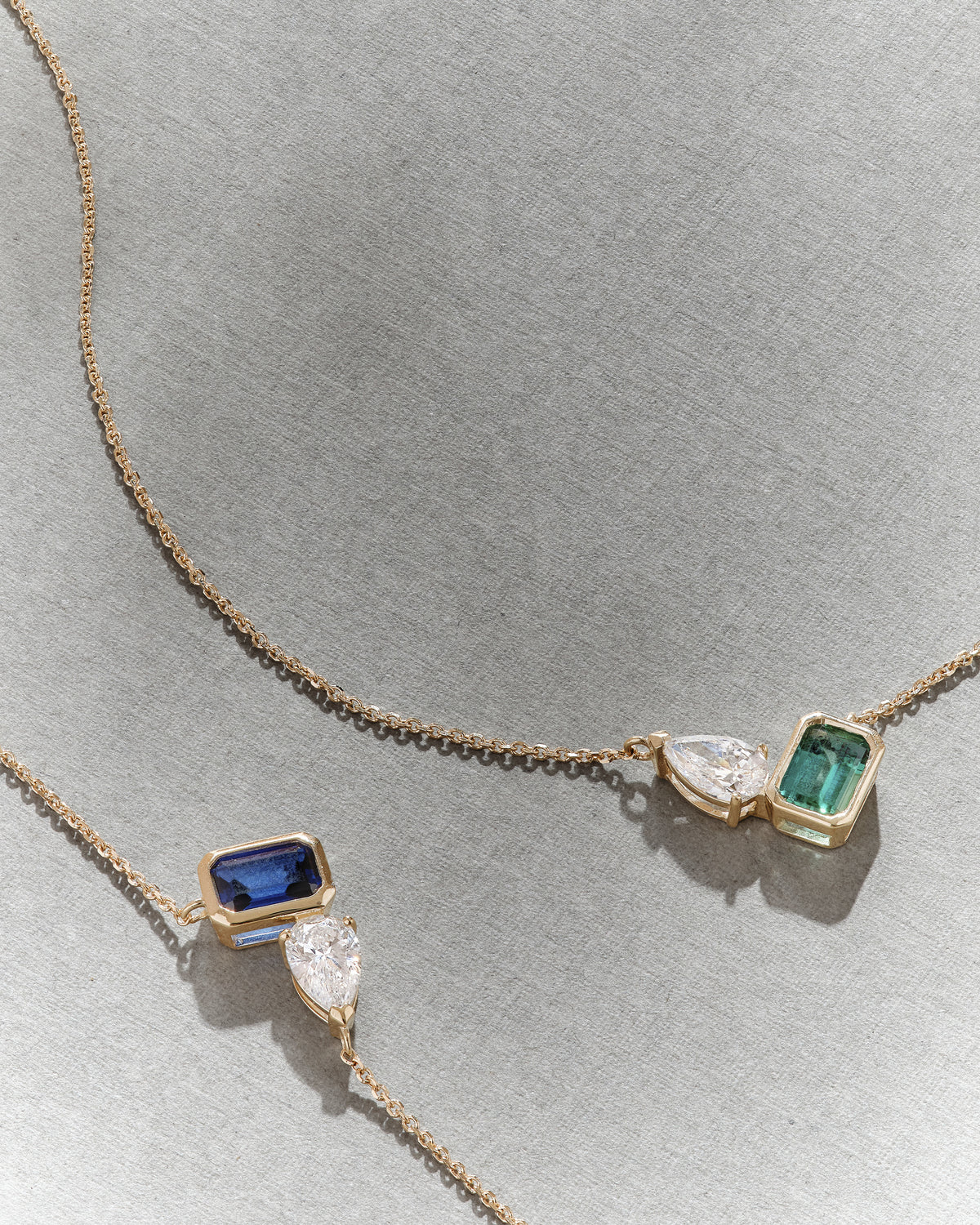 Toi Et Moi Emerald and Diamond Necklace with a gold chain and elegant emerald and diamond pendants displayed on a soft grey background