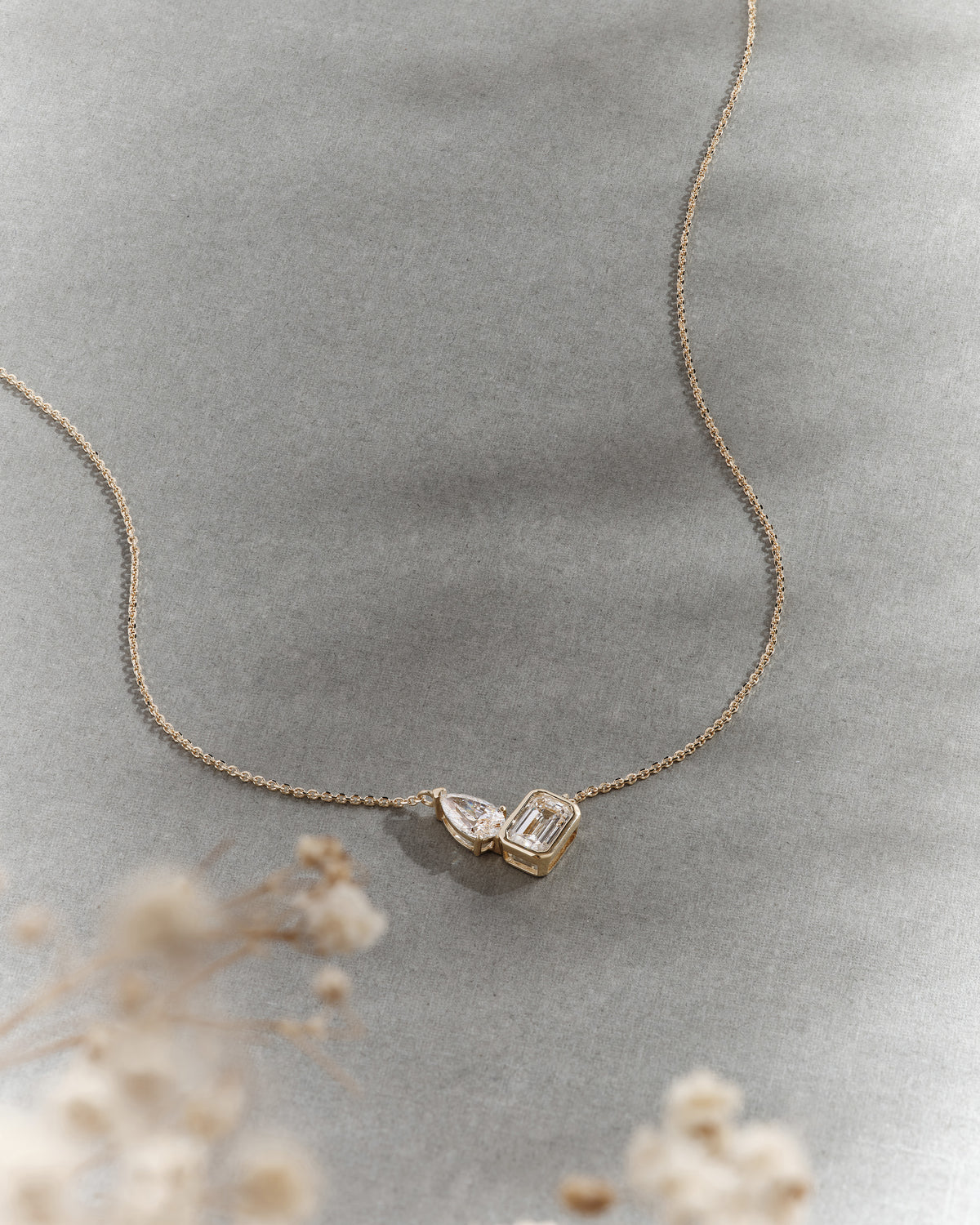 Toi Et Moi Diamond Necklace in gold and diamond with paired pendant details on a delicate chain styled against soft grey fabric