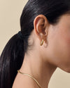 Medium Pebble Hoop Earrings - Gold dangle style worn by a woman with dark hair in a ponytail, showcasing fine jewellery made from recycled metals and solid gold, crafted to last.