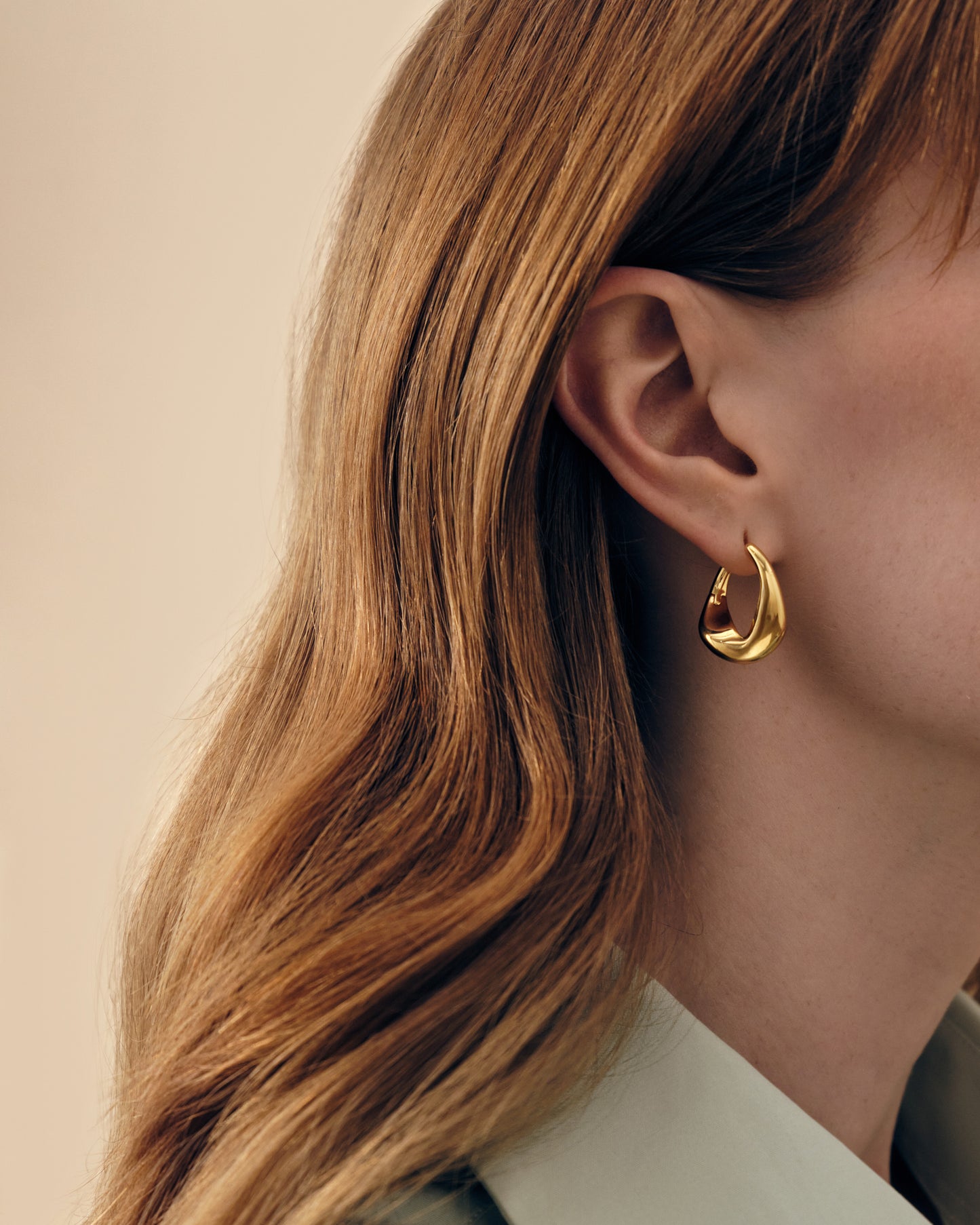 A close-up of a woman wearing Charlotte Collins Large Twist Hoop Earrings in gold-plated sterling silver, showcasing elegant, sustainable, and ethically sourced fine jewellery made from recycled metals.