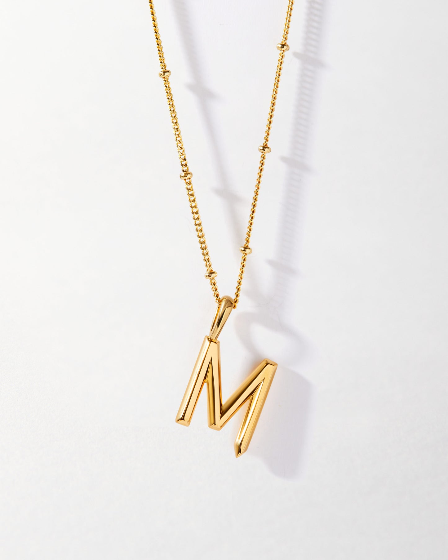 M' Initial Necklace - Gold featuring a polished gold-plated pendant on a delicate chain, crafted with recycled metals and designed as considered fine jewellery for everyday wear.