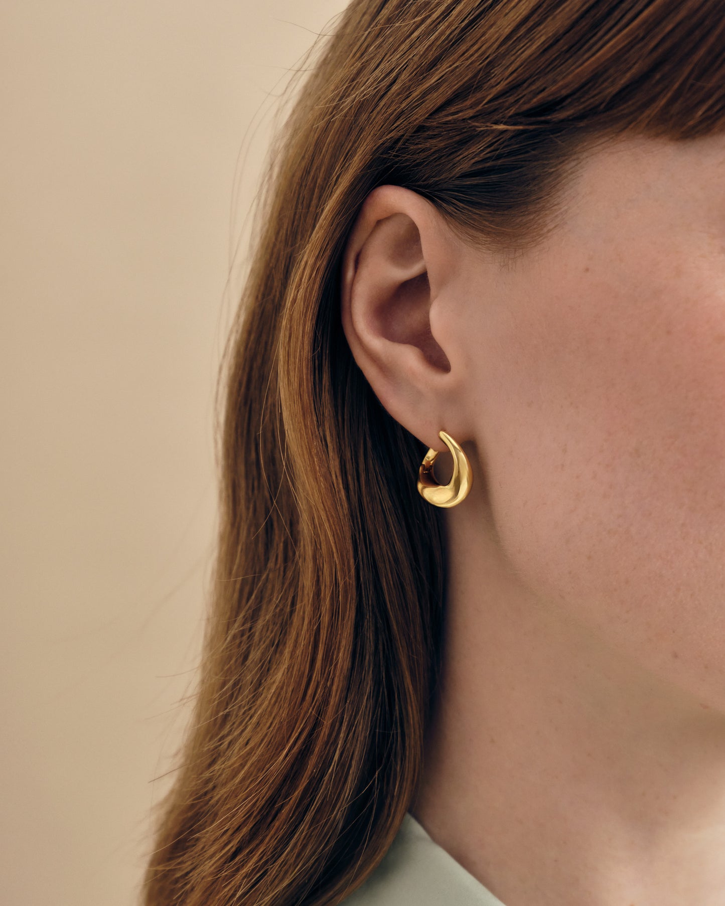 A close-up of a woman wearing Charlotte Collins Medium Twist Hoop Earrings in gold-plated sterling silver, showcasing sustainable, ethically sourced fine jewellery made from recycled metals.