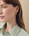 Close-up of a woman wearing Charlotte Collins Medium Twist Hoop Earrings in gold-plated sterling silver, showcasing elegant, sustainable fine jewellery designed for everyday luxury and ethical style.