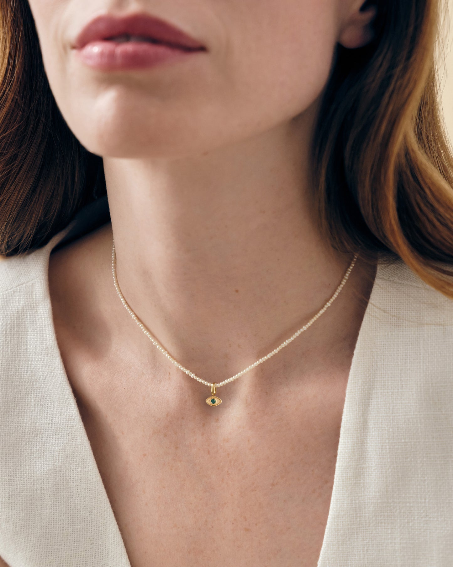 Close-up of a woman wearing a Mini Evil Eye Pearl Necklace featuring a delicate gold-plated pendant on a sterling silver pearl chain, perfect for adding subtle elegance.