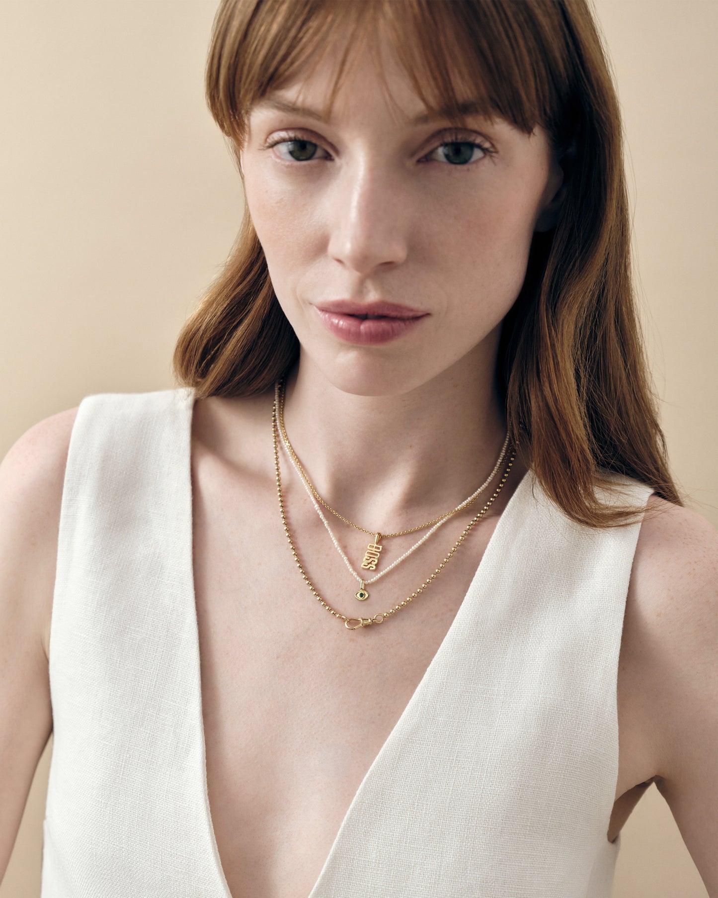 Close-up of a woman wearing the Mini Evil Eye Pearl Necklace in gold-plated sterling silver with a delicate pearl pendant and chain, styled with layered necklaces and a white top.