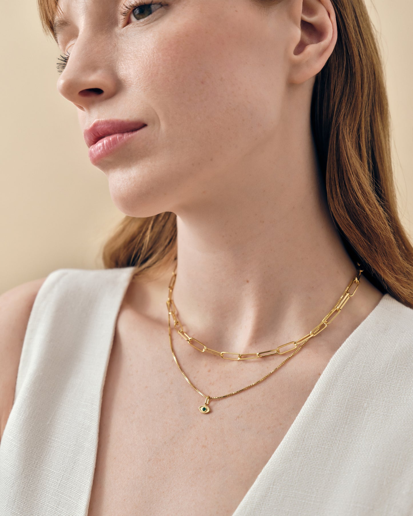 Close-up of a woman wearing a gold-plated Mini Evil Eye Necklace with a delicate pendant on a fine chain, styled with a second layered gold chain, showcasing affordable luxury fine jewellery.
