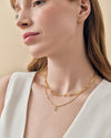 Close-up of a woman wearing a gold-plated Mini Evil Eye Necklace with a delicate pendant on a fine chain, styled with a second layered gold chain, showcasing affordable luxury fine jewellery.