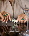 Close-up of hands wearing multiple Charlotte Collins Malachite Statement Rings in gold-plated sterling silver, holding a domino piece on a reflective surface, showcasing sustainable fine jewellery.