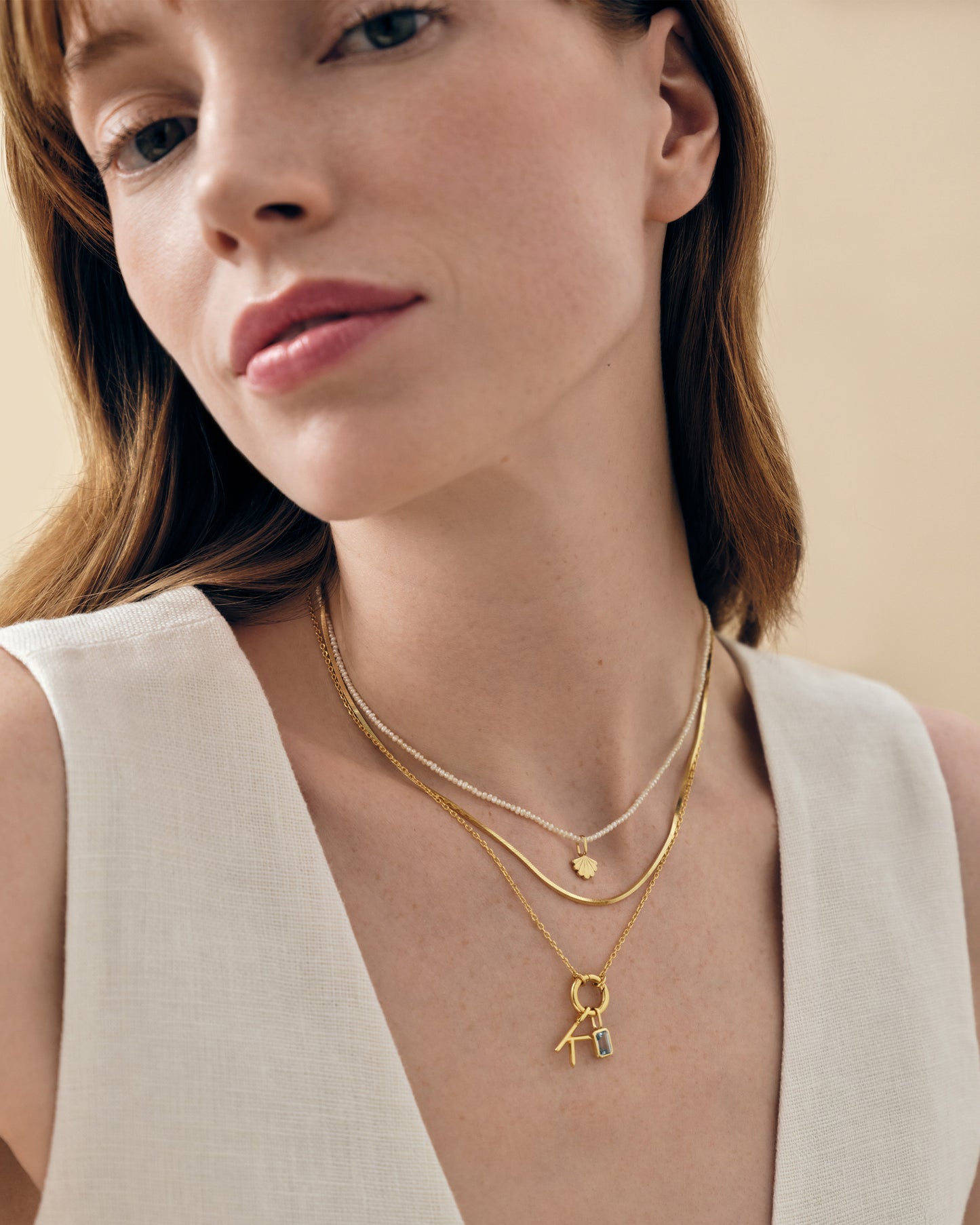 Close-up of a woman wearing layered gold-plated and sterling silver necklaces featuring a delicate Mini Shell Pearl Necklace pendant, showcasing ethically sourced fine jewellery crafted from recycled metals with elegant chain designs.