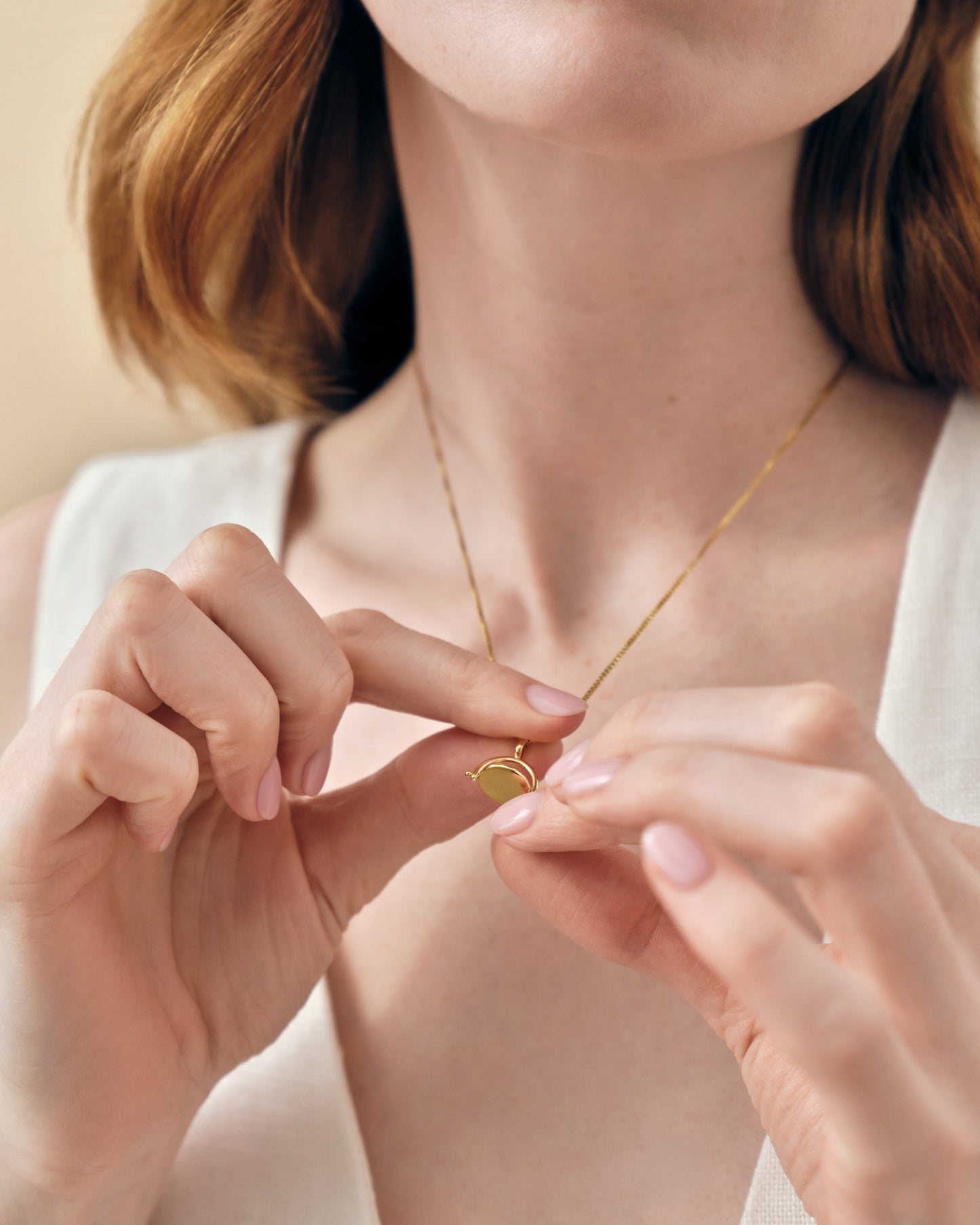 Close-up of a woman wearing and gently holding a Mini Spinner Pendant necklace in gold-plated finish, showcasing considered jewellery made in recycled metals, built to last.