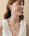 A smiling woman wearing a delicate gold chain necklace featuring the Mini Deco Birthstone Pendant with colorful birthstones, crafted from gold-plated and sterling silver materials, showcasing considered jewellery made from recycled metals and ethical sourcing.