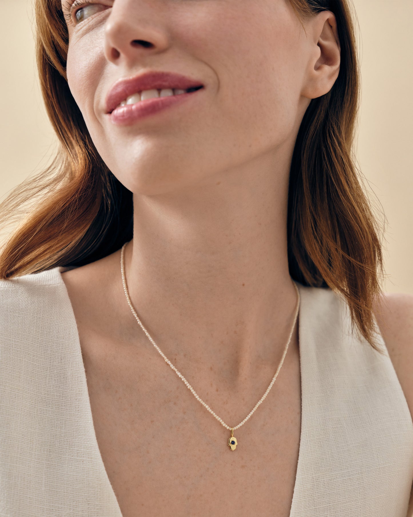 Woman wearing a delicate Mini Hamsa Pearl Necklace featuring a gold-plated pendant on a fine chain, showcasing affordable luxury crafted from recycled metals and ethically sourced materials.