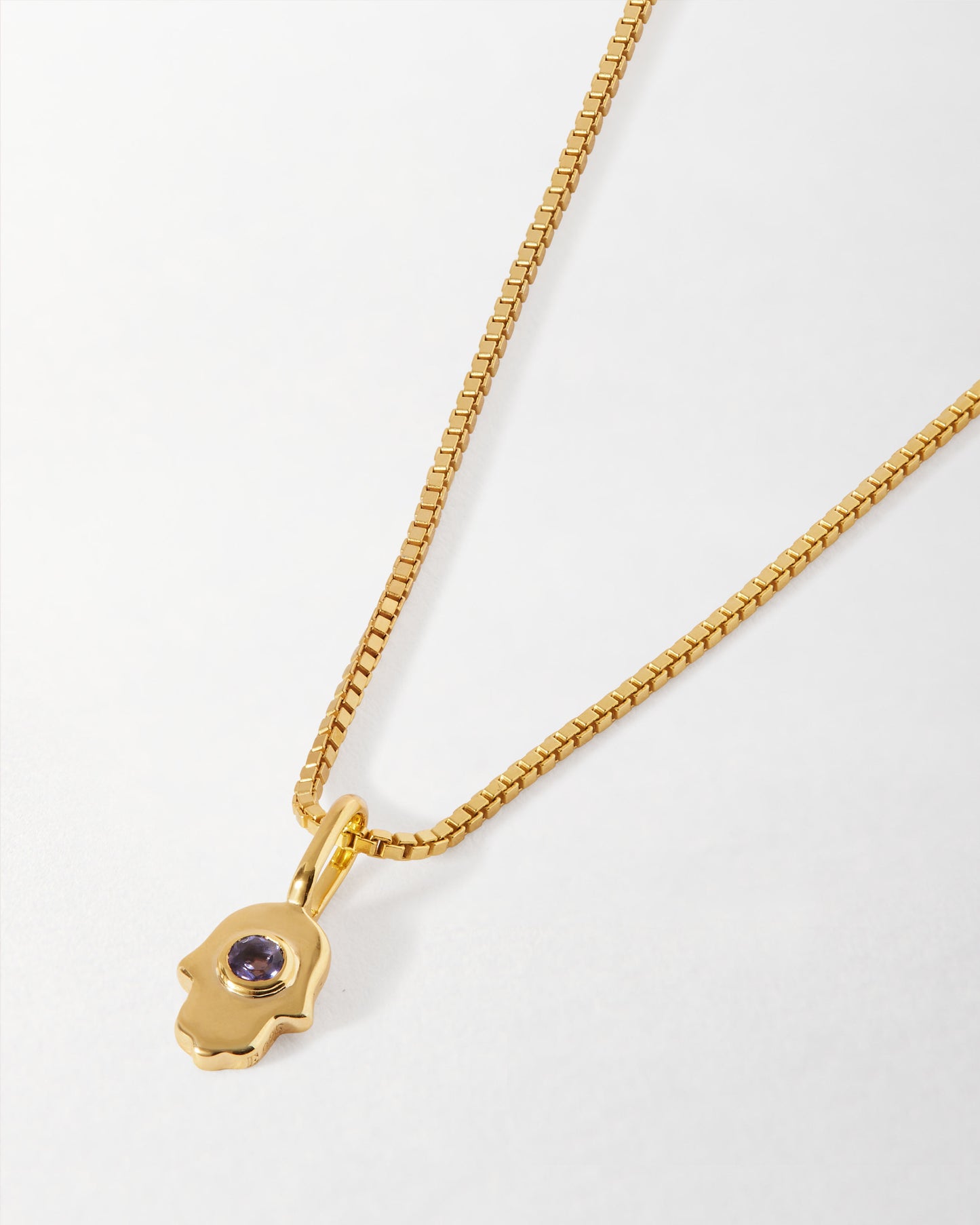 Mini Hamsa Necklace featuring a gold-plated pendant with a purple gemstone on a matching chain, crafted from recycled metals and designed for everyday fine jewellery wear.