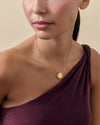 Woman wearing a gold-plated Secret Message Locket Necklace with a pendant and chain, styled with a purple off-shoulder top, showcasing considered jewellery made from recycled metals.