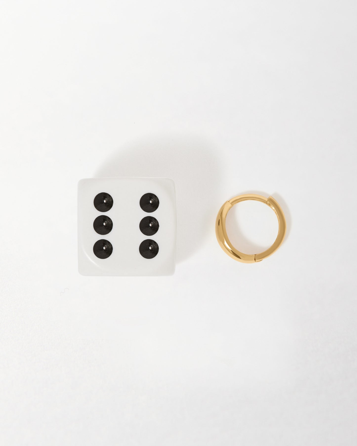 Bold Huggie Earrings - Yellow Gold displayed beside a six-sided die, showcasing solid gold craftsmanship with recycled metals and ethical sourcing in a minimalist style.