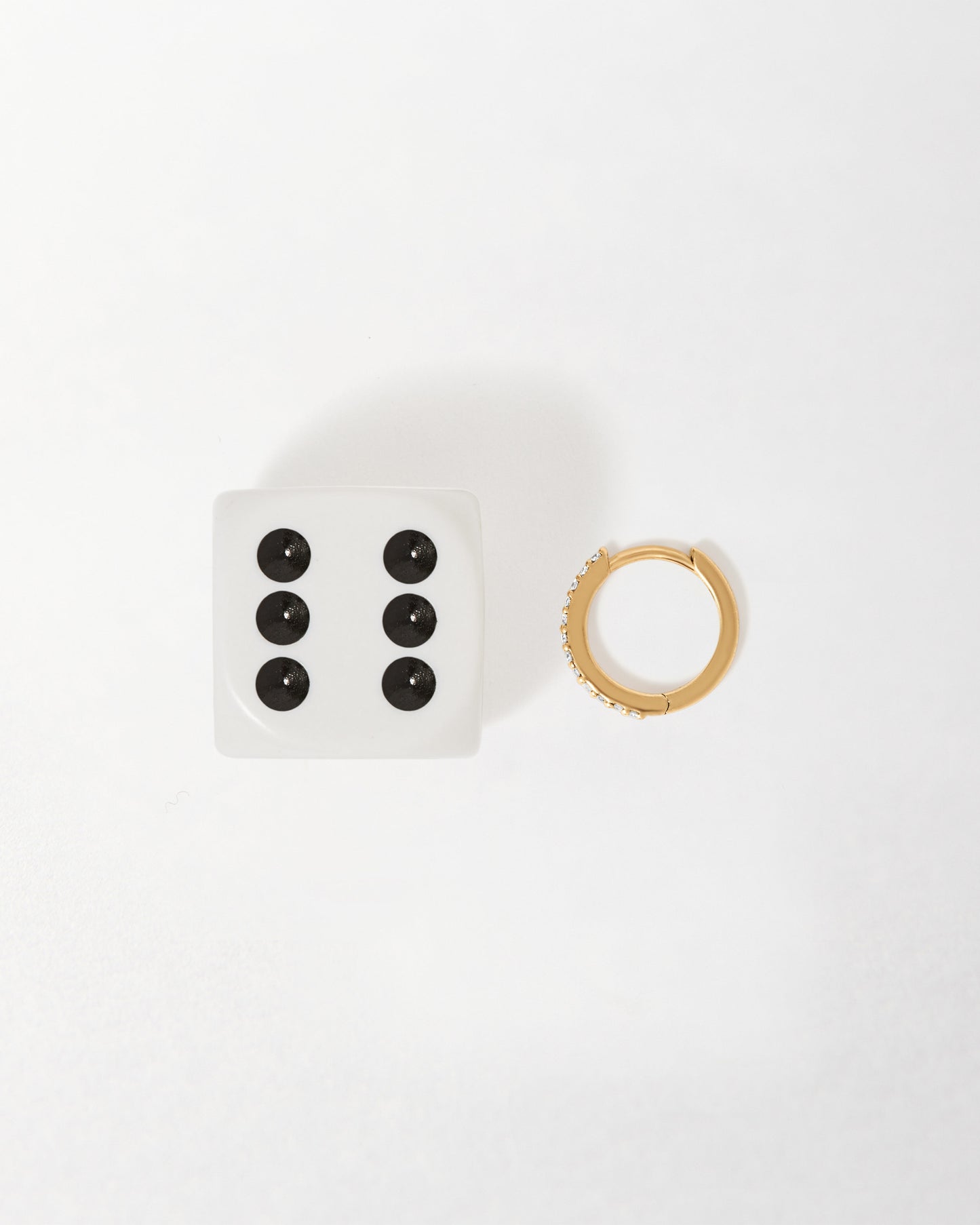Pavé Diamond Huggies - Yellow Gold earring displayed beside a white dice showing six black dots, highlighting fine 14ct solid gold craftsmanship with ethical sourcing and recycled metals.