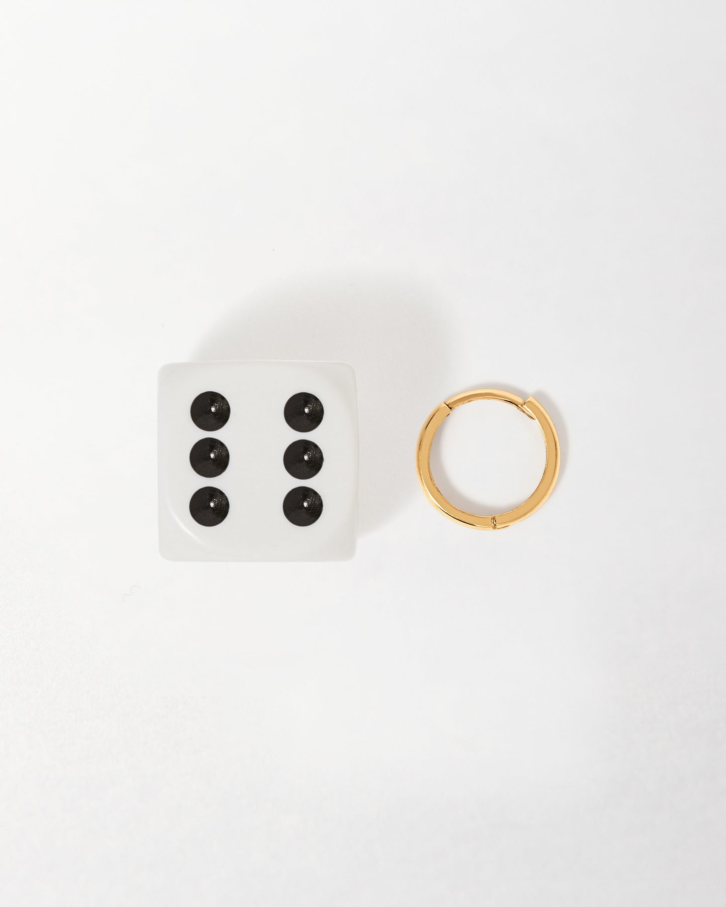 A single Solid Gold Huggie Hoop Earrings displayed next to a white six-sided die, showcasing fine craftsmanship in recycled 14ct gold, embodying considered, ethical jewellery.