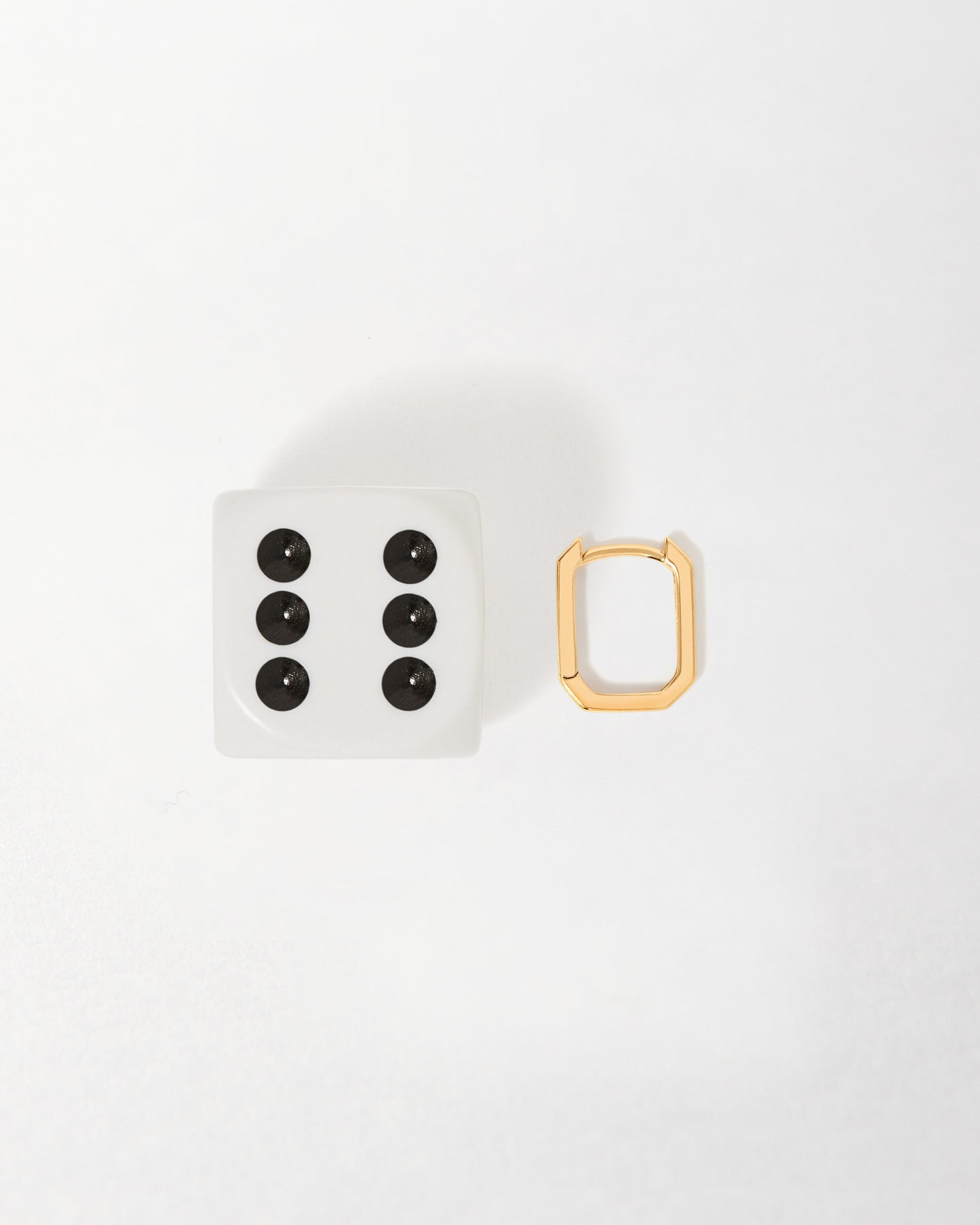 Solid Gold Mini Deco Hoop Earrings displayed beside a white six-sided die, highlighting their sleek, geometric huggie design crafted with sustainable solid gold for everyday fine jewellery.