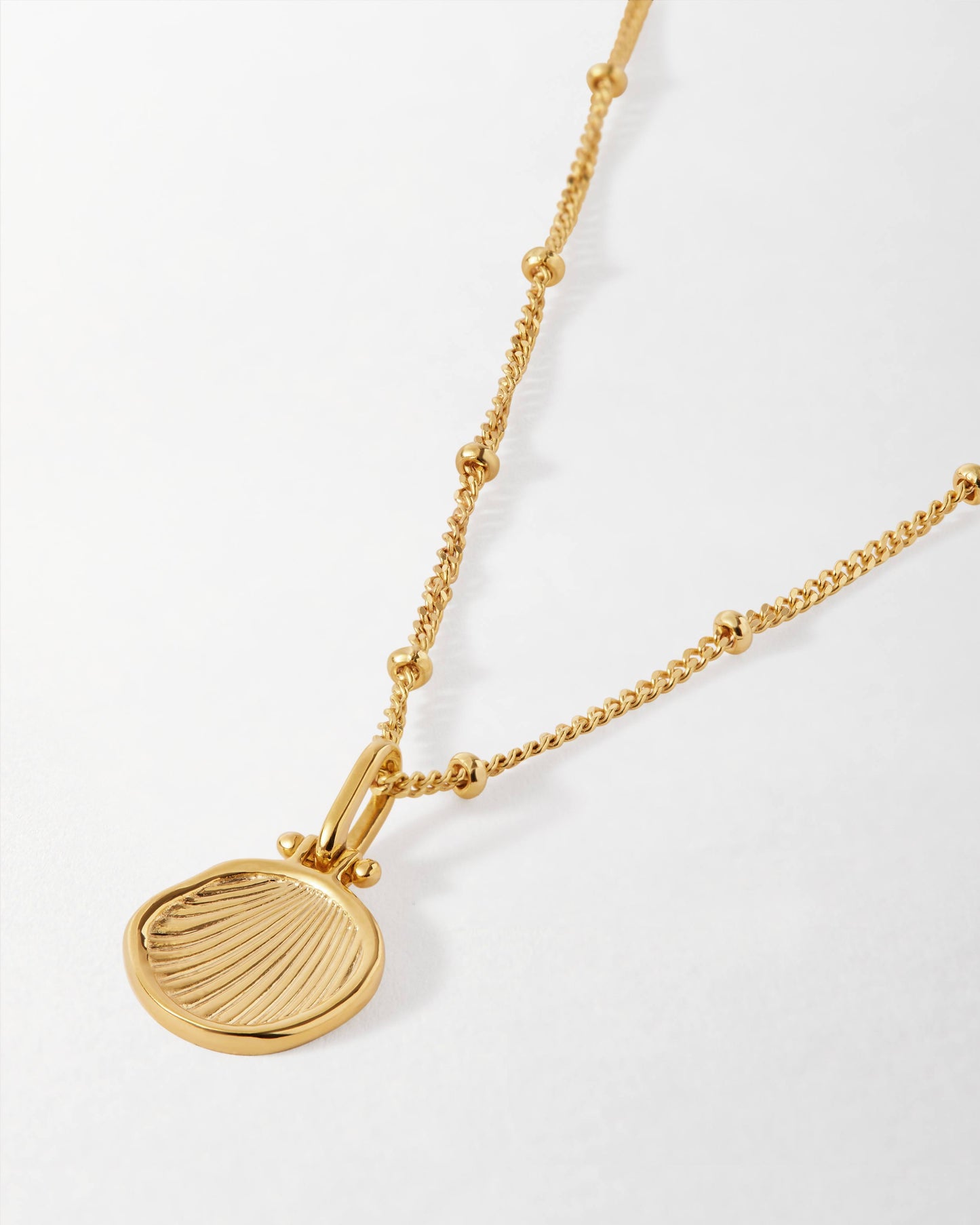 Close-up of a Coastal Shell Necklace featuring a gold-plated pendant with shell detailing on a delicate chain with small beads, crafted with recycled metals for sustainable fine jewellery.